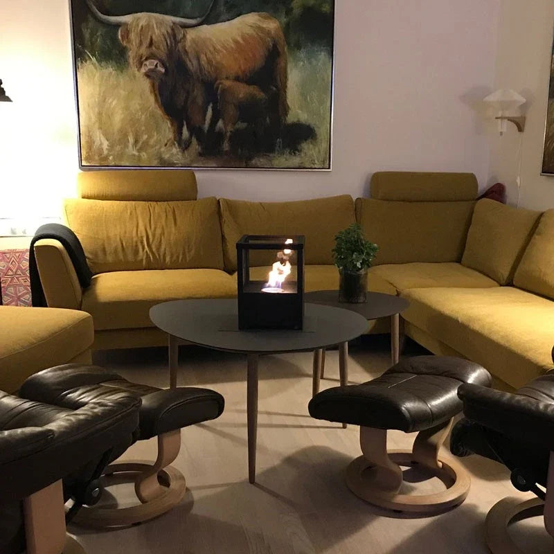 Square black tabletop bioethanol fireplace lit on a coffee table in a cozy living room with mustard sofa